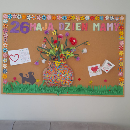Własnoręcznie_wykonana_tablica_z_okazji_Dnia_Matki_na_której_przedstawiony_jest_wazon_z_kwiatami_laurki_matka_z_dzieckiem_oraz_trawa_i_kwiaty.png
