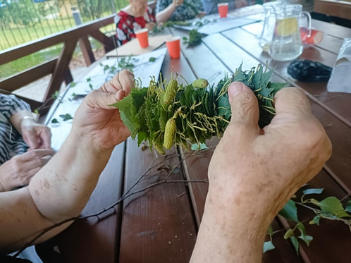 Zdjęcie_nr_9_przedstawia_zajęcia_z_arteterapii_na_świeżym_powietrzu_podczas_których_seniorzy_tworzyli_wianki_z_liści_brzozy.png