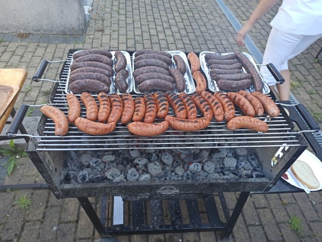  Na głównym planie mamy grilla a na nim kiełbasy i kaszanki. Grill jest odpalany metoda tradycyjną - na węgiel.