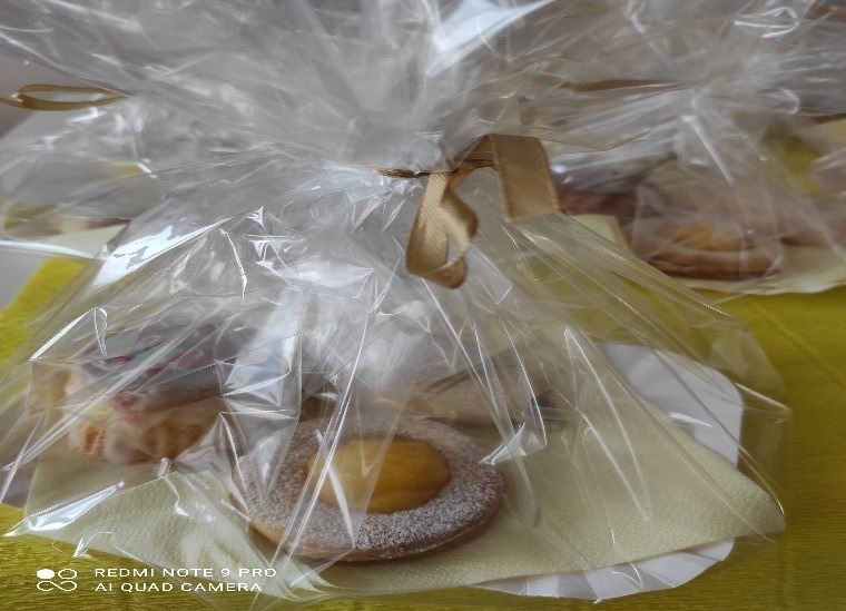 Słodkie poczęstunki- ciastka, na tekturowych talerzykach, zapakowane w przeźroczystą folię prezentową, przewiązane wstążką