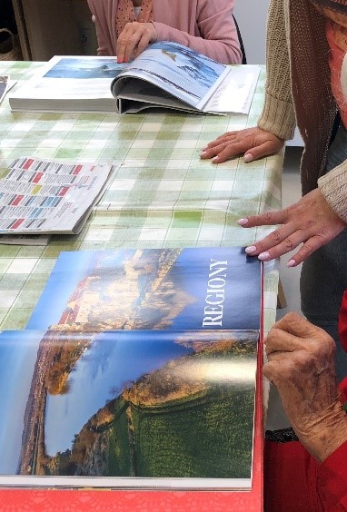 Fotografia Przedstawia stółpokryty obrusem w biało-zieloną kratkę. Na stole znajdują się otwarte książki – albumy z fotografiami przyrody