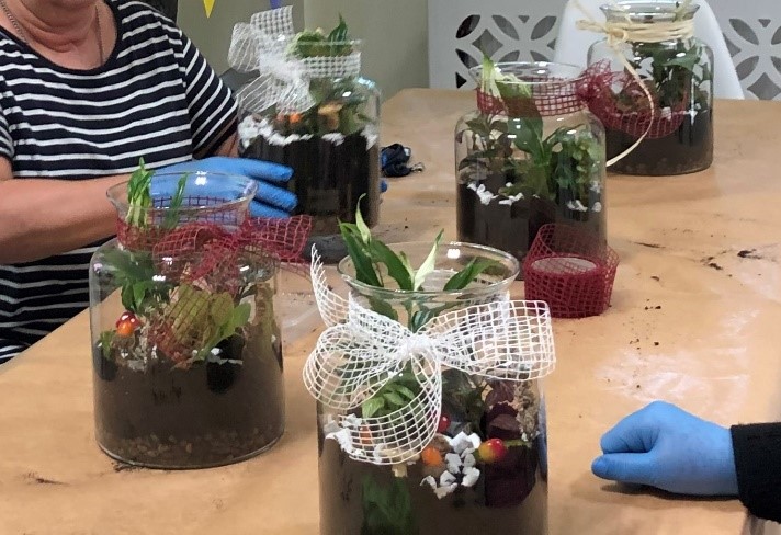Przedstawia efekt wykonanych „Ogrodów w słoiku”. 5 pięknie udekorowanych szklanych naczyń, w których znajdują się rośliny i różnego rodzaju ozdoby florystyczne.