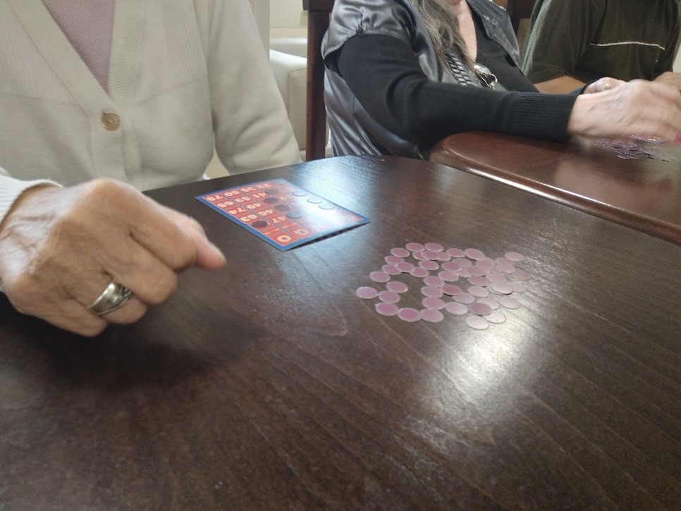 Na zdjęciu widać jak mieszkanka siedzi przy stole i gra w Bingo